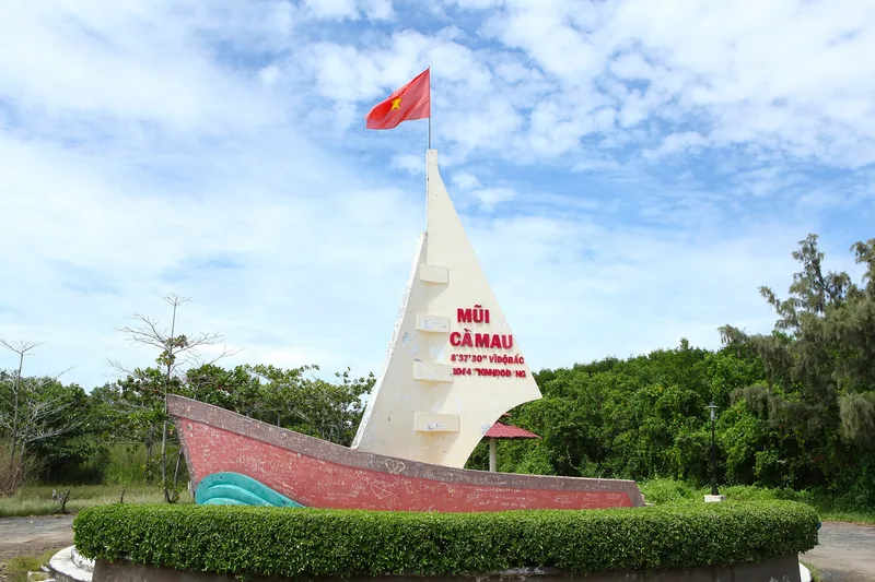 Cột mốc hình con thuyền đánh dấu Mũi Cà Mau, điểm cực Nam Việt Nam, dưới bầu trời xanh với quốc kỳ tung bay.