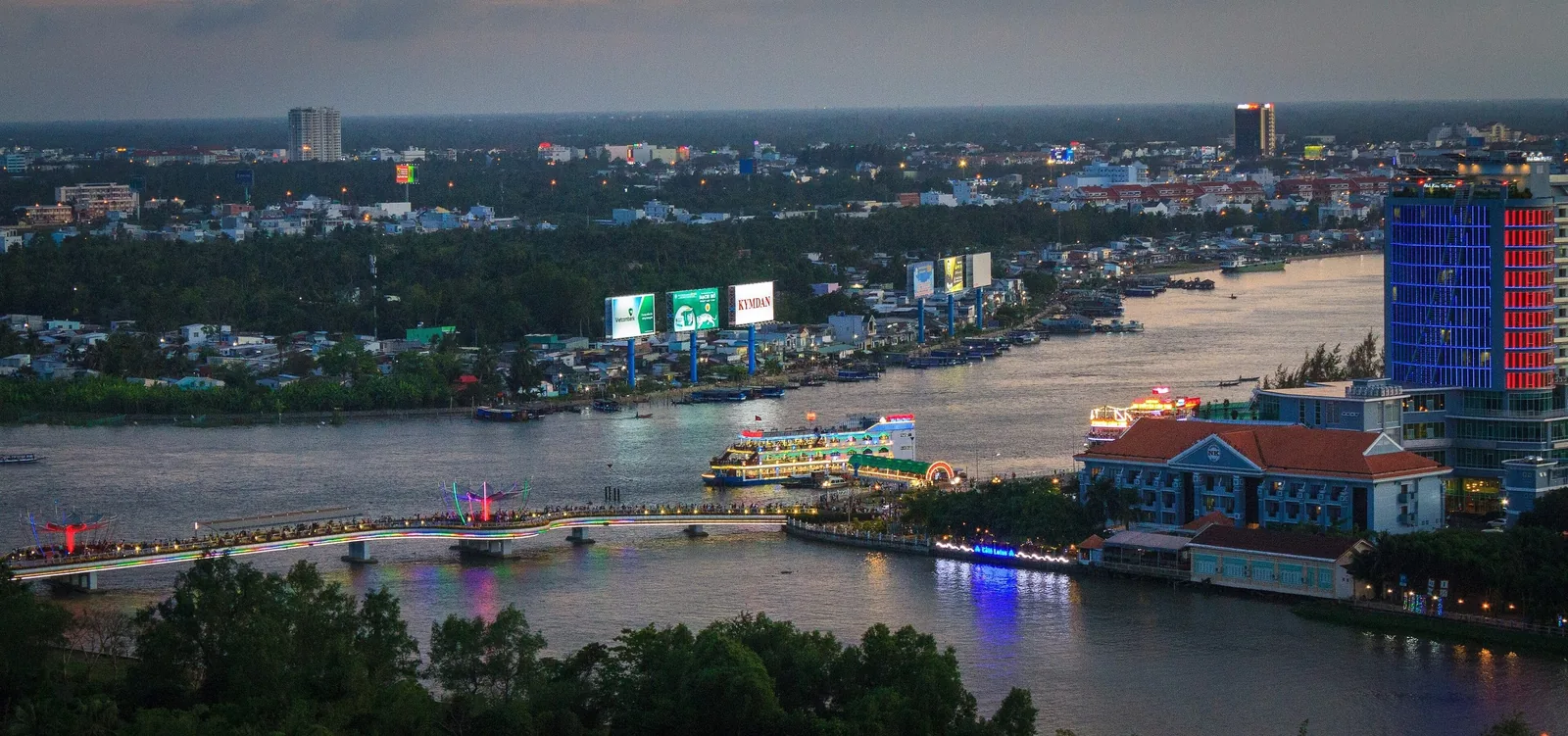 Toàn cảnh thành phố Cần Thơ lúc chạng vạng với dòng sông, cầu và các tòa nhà bên bờ sáng đèn.