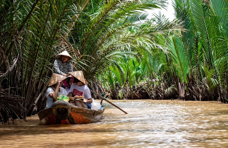Người chèo thuyền đưa du khách đội nón lá qua rạch nước dừa nước rợp bóng ở Đồng bằng sông Cửu Long.