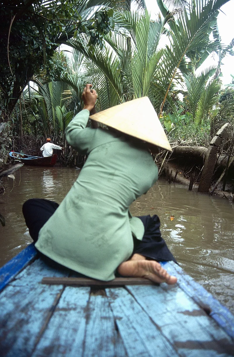 Người phụ nữ đội nón lá chèo xuồng gỗ qua con rạch nhỏ rợp bóng dừa nước ở Đồng bằng sông Cửu Long.