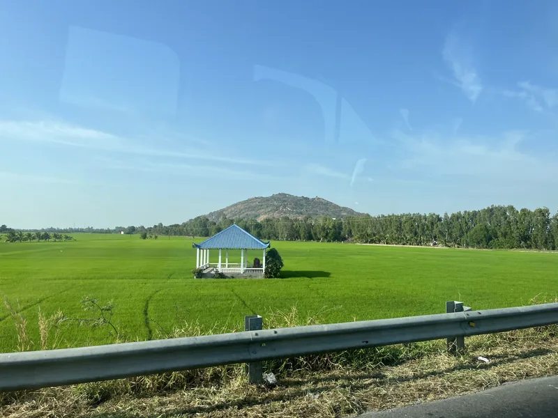 Một nhà lục giác mái xanh nằm giữa ruộng lúa xanh mướt với ngọn núi nhỏ phía sau ở Đồng bằng sông Cửu Long.